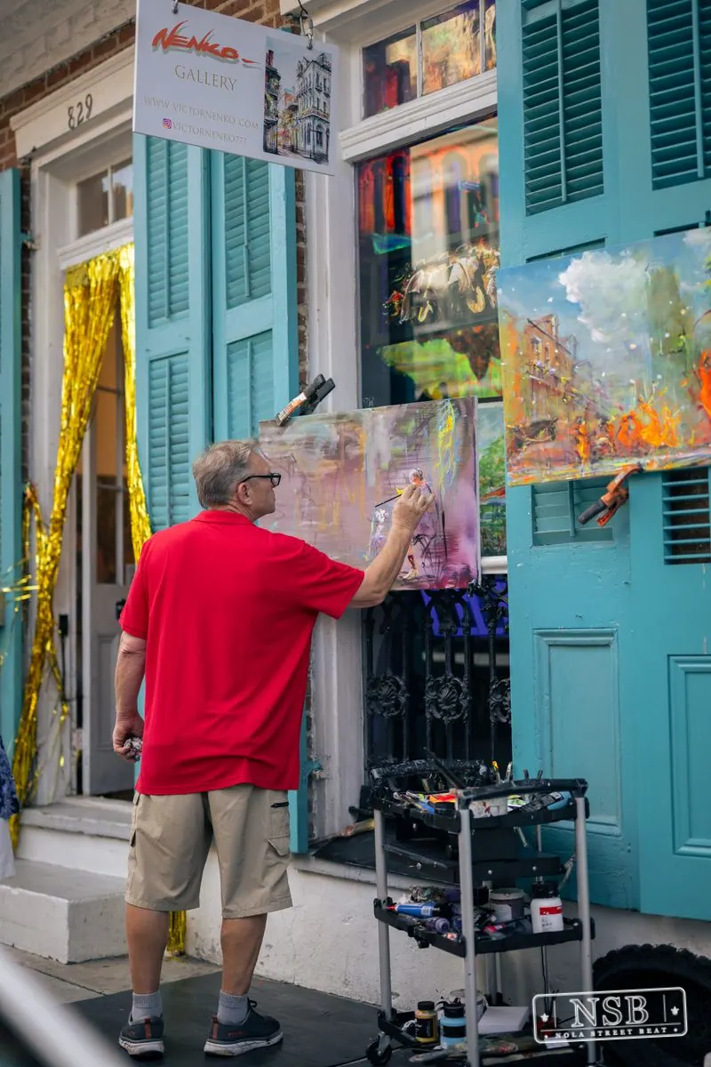 Artist painting beside a colorful Royal Street storefront during Dirty Linen Night 2026