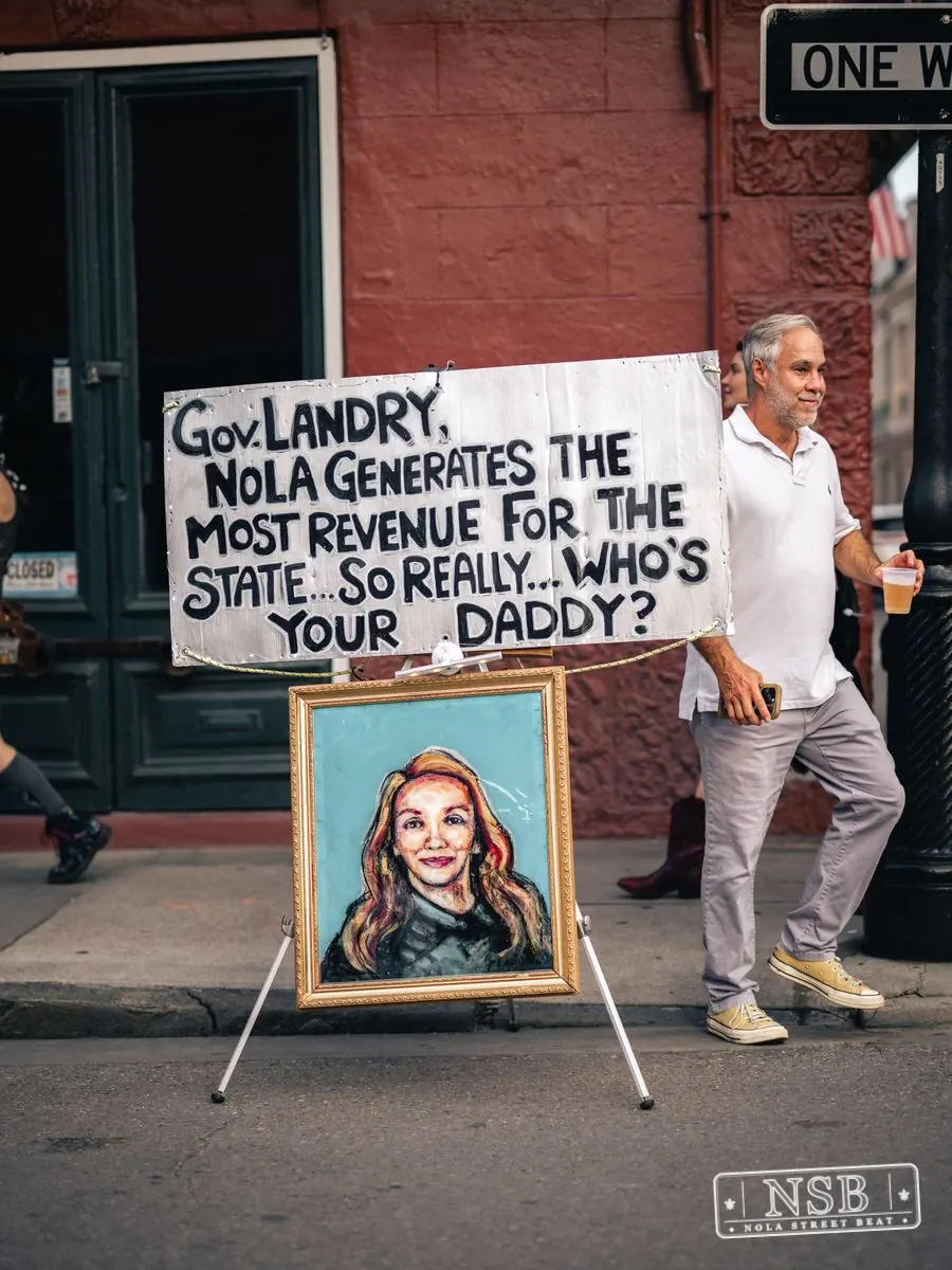 Street portrait with a hand-lettered sign during Dirty Linen Night 2026 on Royal Street