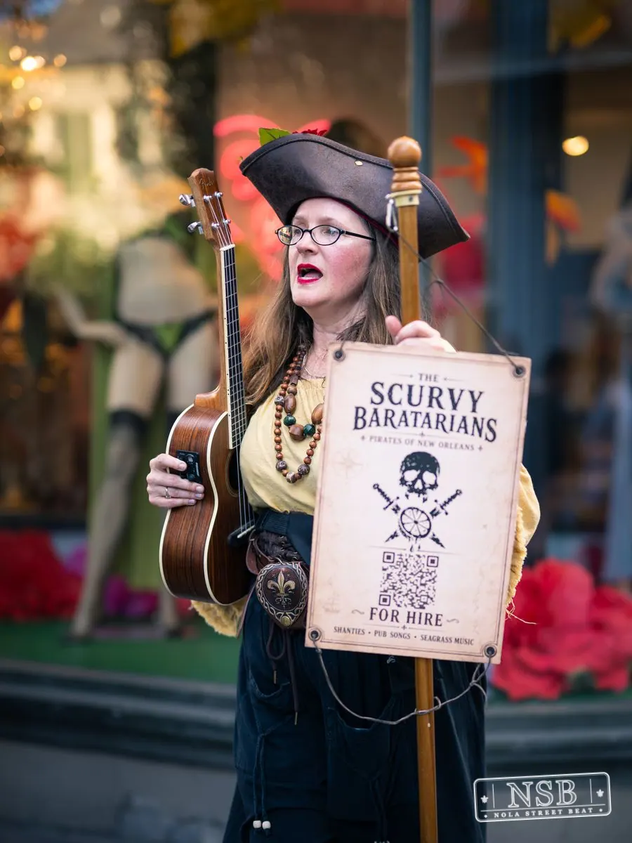 Street performer holding a handmade sign at Dirty Linen Night 2026