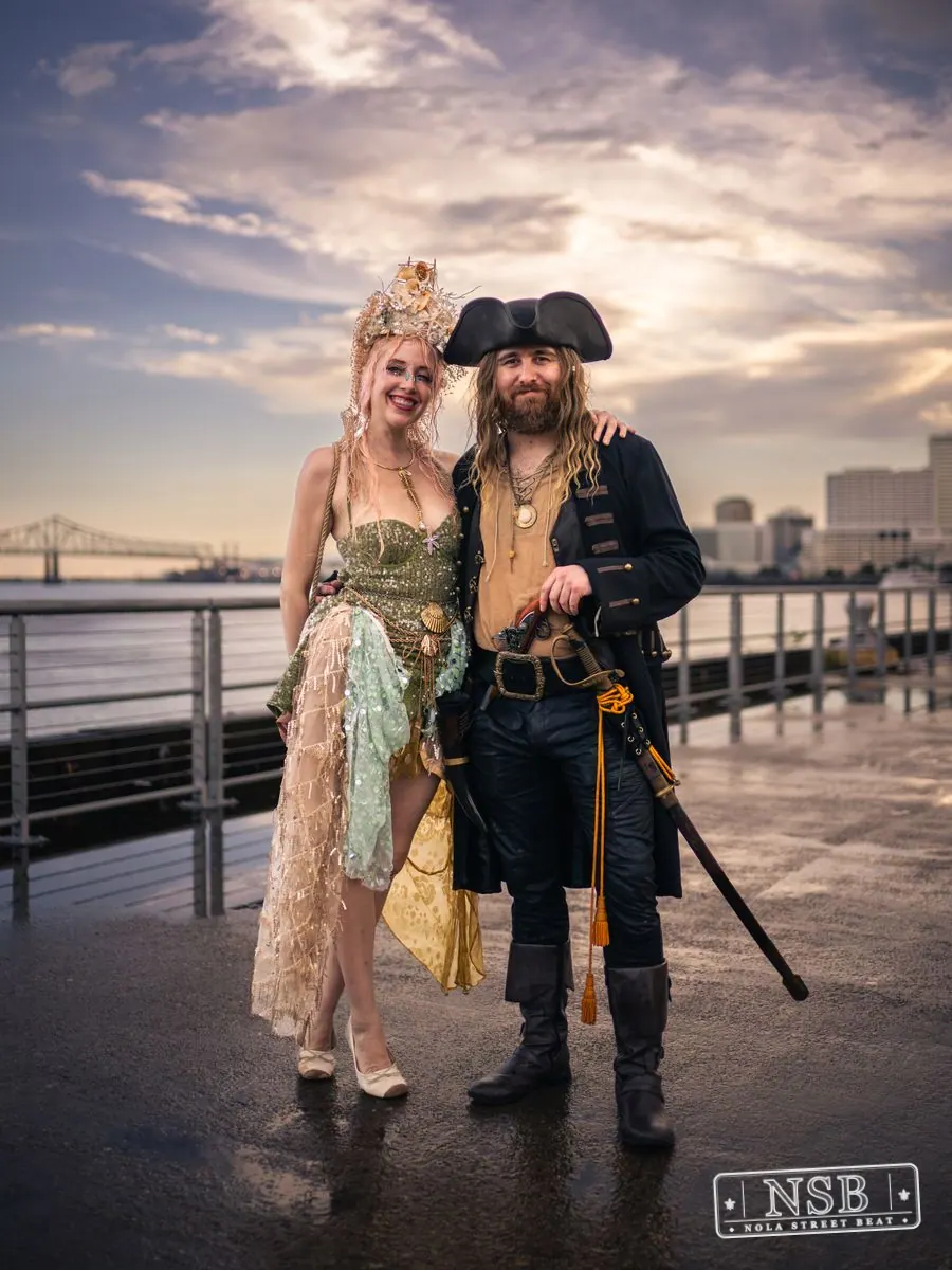 A mermaid and pirate posing together beside the Mississippi River at the 2026 New Orleans Mermaid Parade