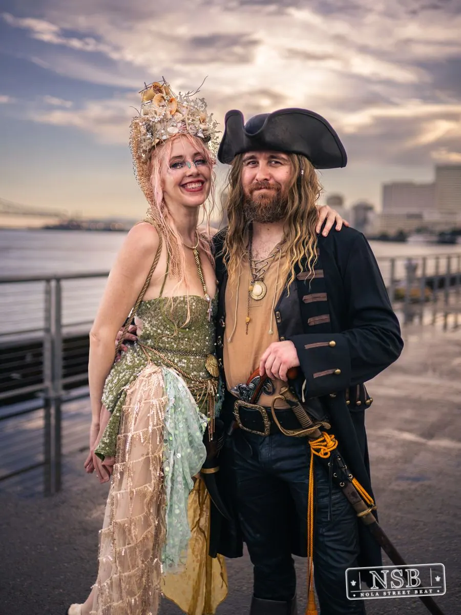 A mermaid and pirate posing together beside the Mississippi River at the 2026 New Orleans Mermaid Parade