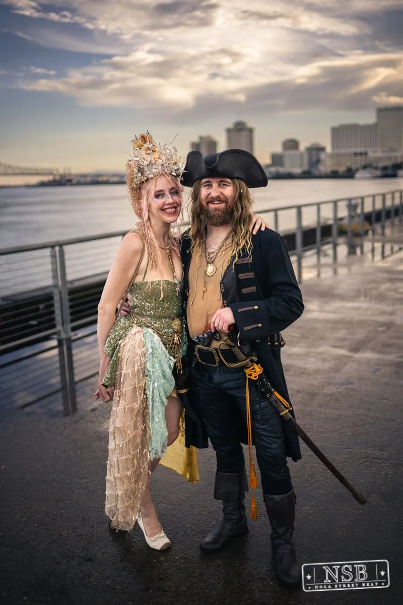 A mermaid and pirate posing together beside the Mississippi River at the 2026 New Orleans Mermaid Parade