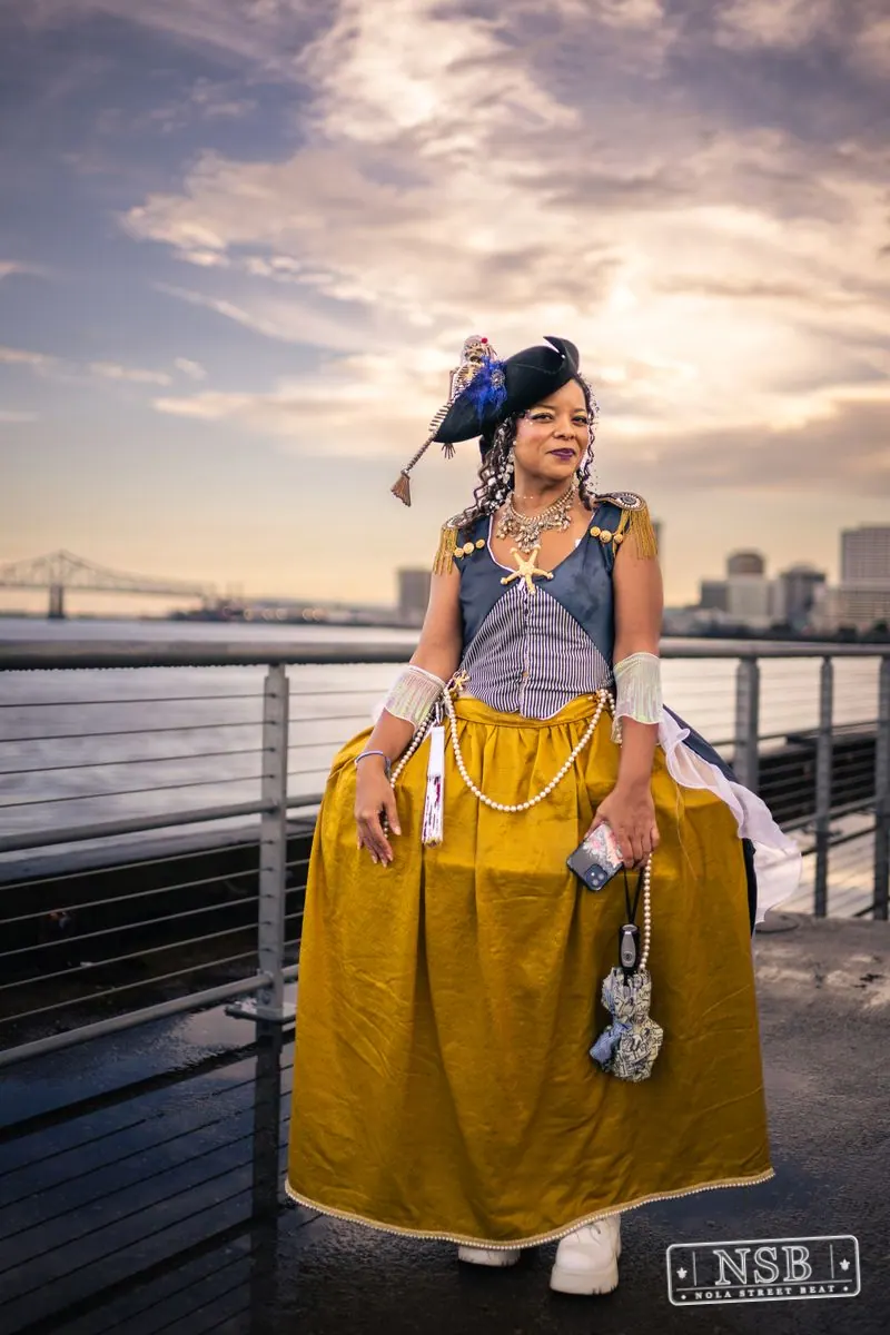 A costumed parade participant wearing a yellow skirt and blue feathered hat at the 2026 New Orleans Mermaid Parade