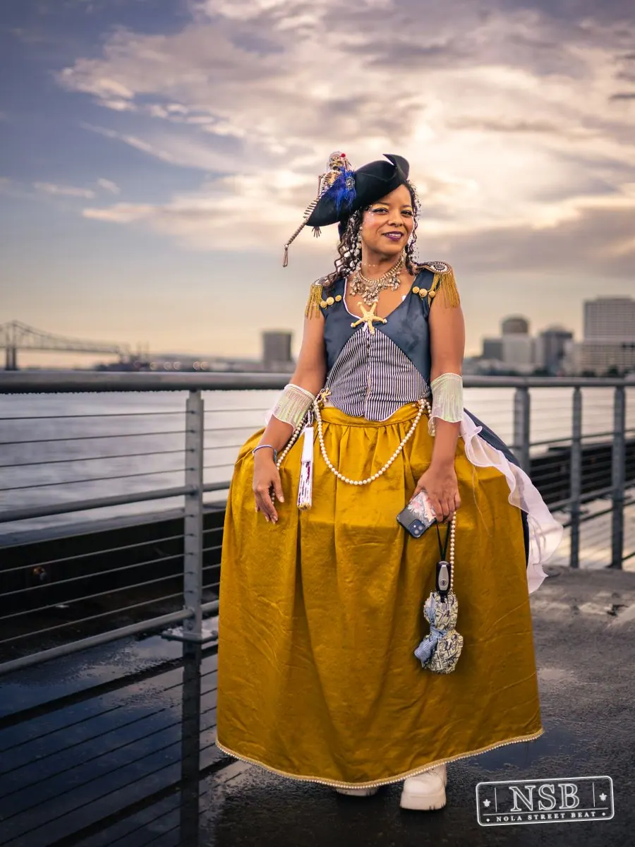 A costumed parade participant wearing a yellow skirt and blue feathered hat at the 2026 New Orleans Mermaid Parade