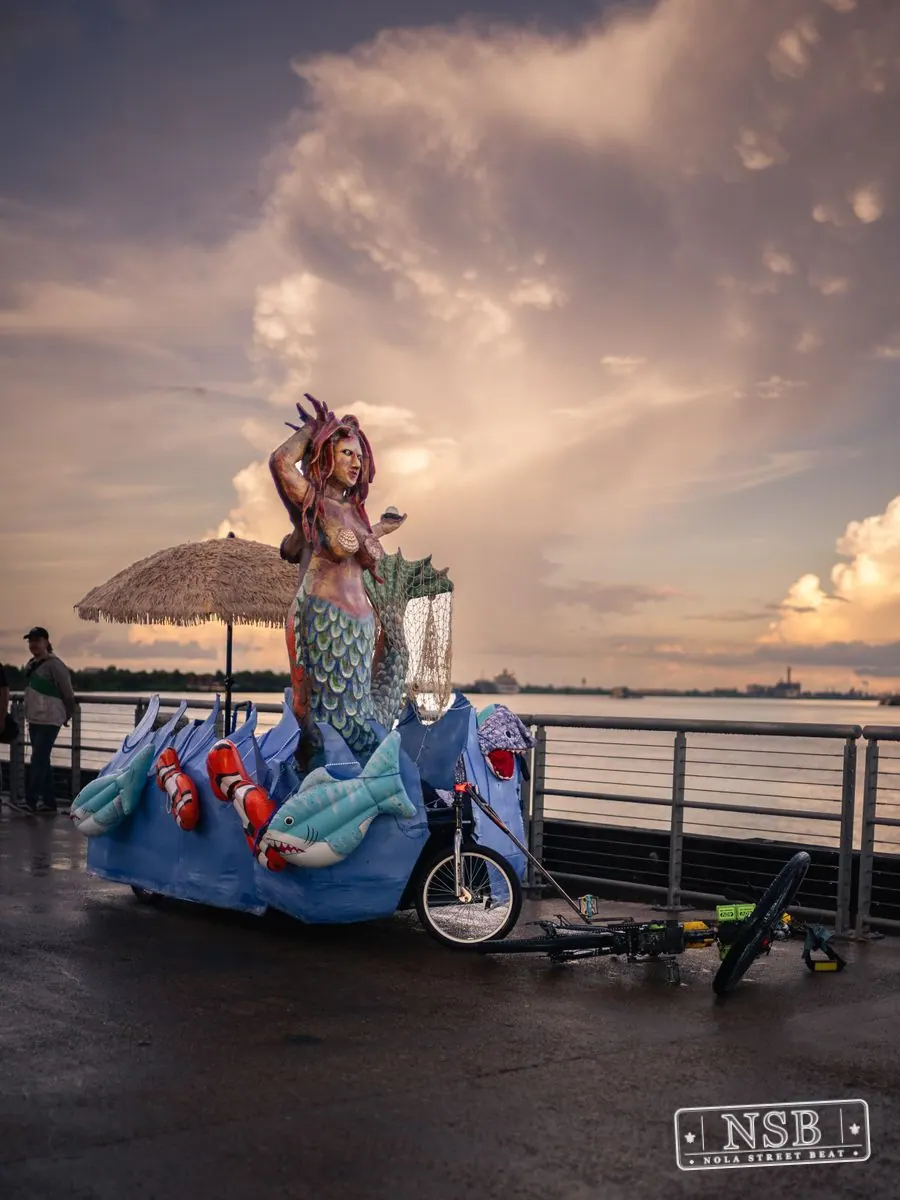 A towering mermaid figure and decorated bicycles along the riverfront at the 2026 New Orleans Mermaid Parade