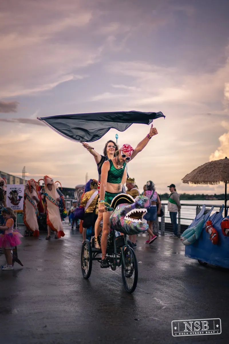A towering mermaid figure and decorated bicycles along the riverfront at the 2026 New Orleans Mermaid Parade