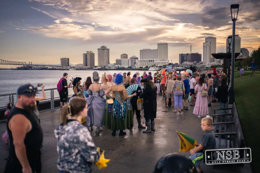 Mermaid Parade participants gathering beside the river under an evening sky at the 2026 New Orleans Mermaid Parade