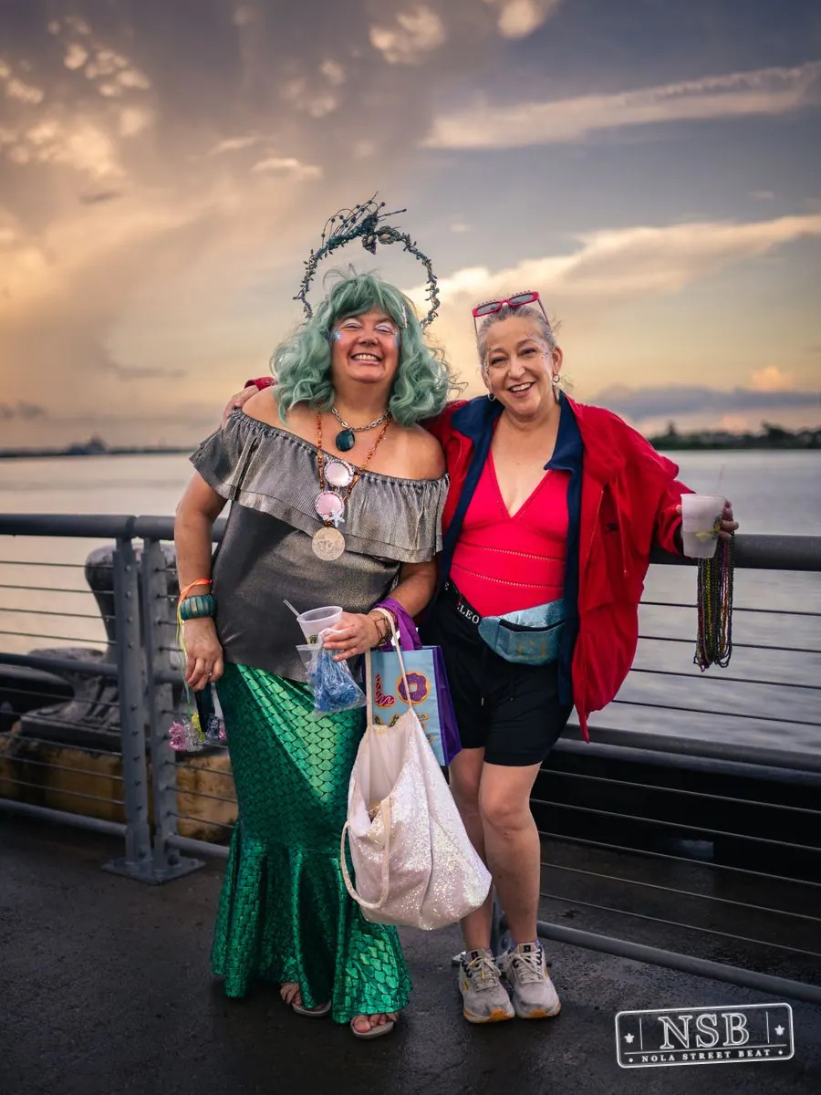 Two costumed participants posing beside the river at the 2026 New Orleans Mermaid Parade