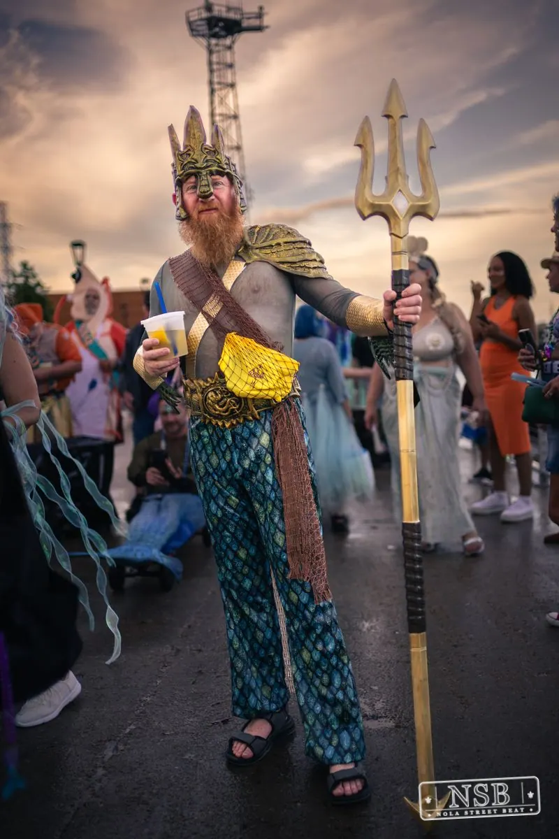 A crowned sea-themed parade participant carrying a trident at the 2026 New Orleans Mermaid Parade