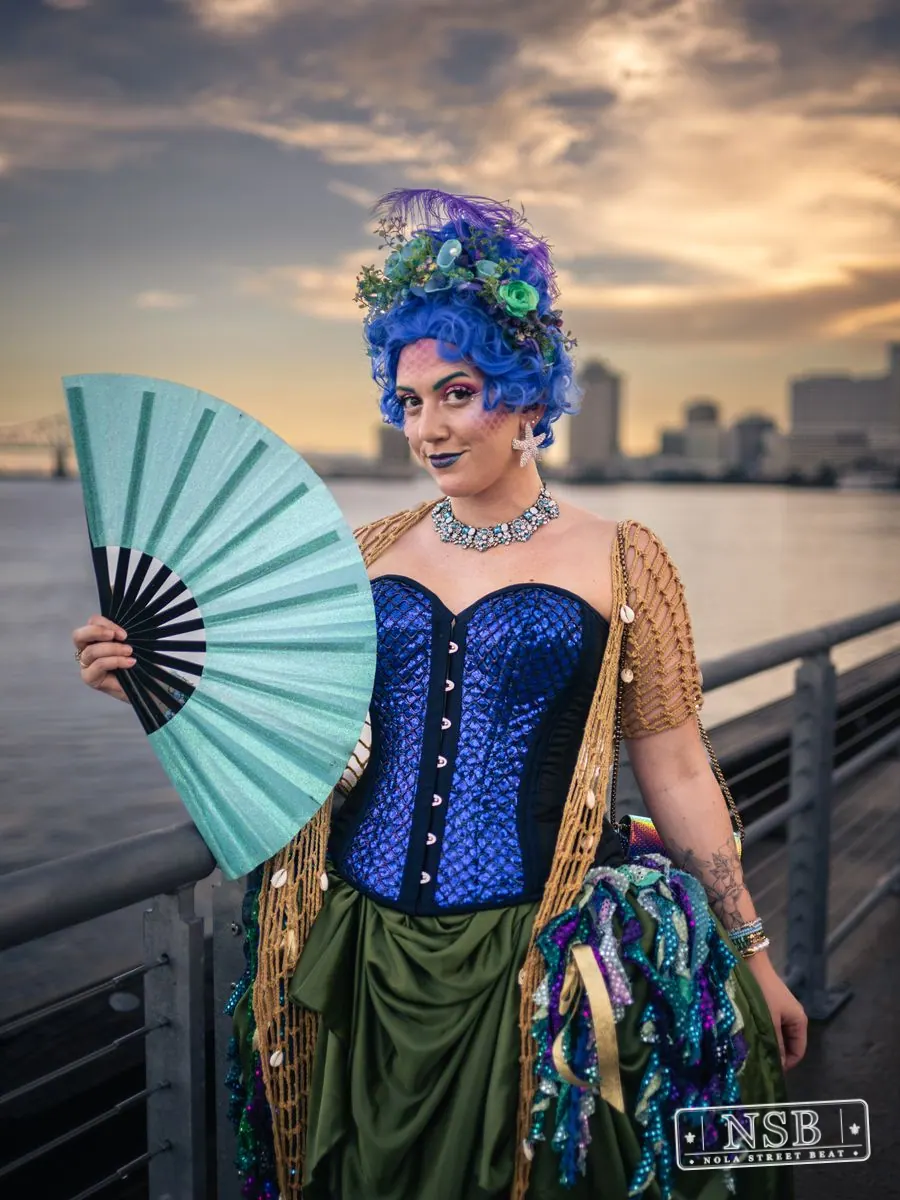 A participant in a blue corset and sea-inspired crown holding a blue fan at the 2026 New Orleans Mermaid Parade