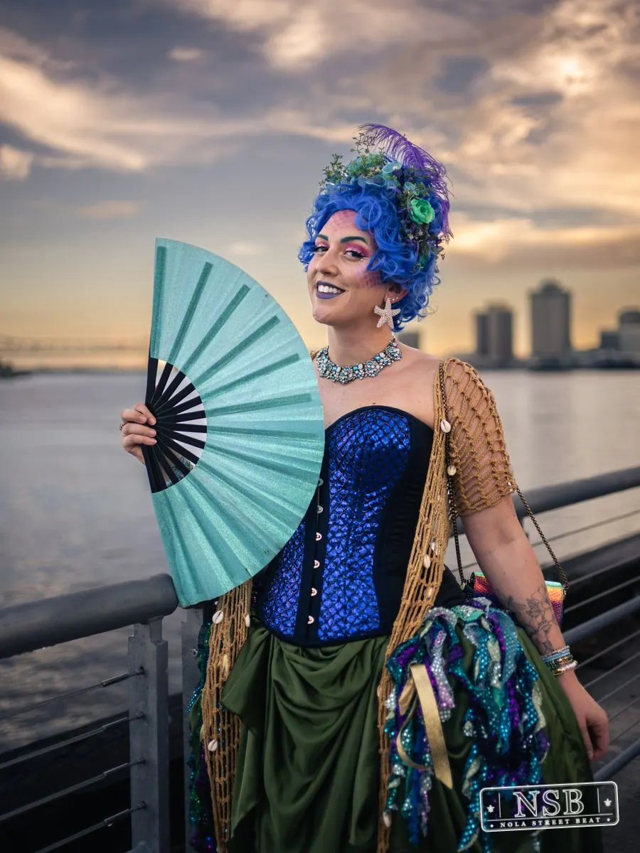 A participant in a blue corset and sea-inspired crown holding a blue fan at the 2026 New Orleans Mermaid Parade