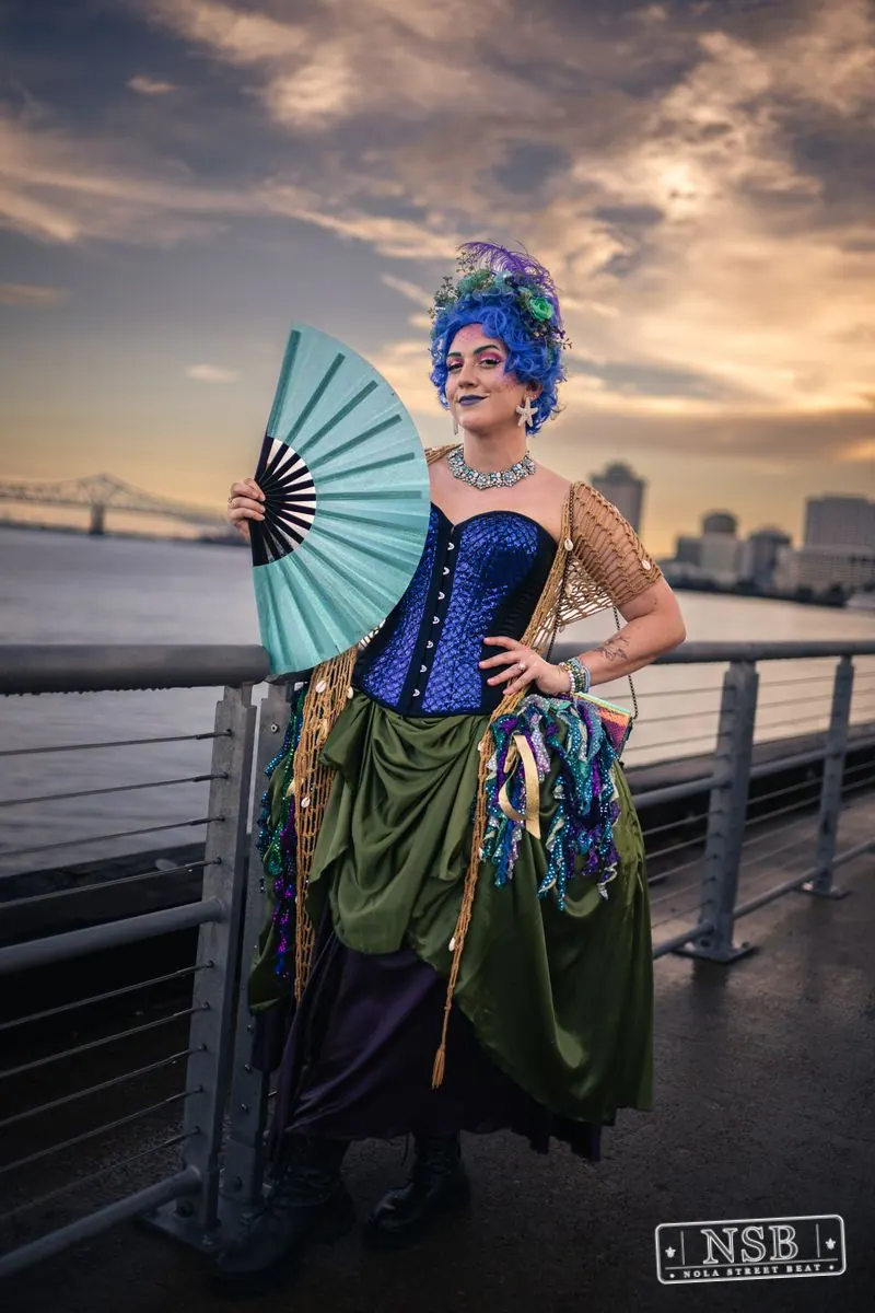 A participant in a blue corset and sea-inspired crown holding a blue fan at the 2026 New Orleans Mermaid Parade