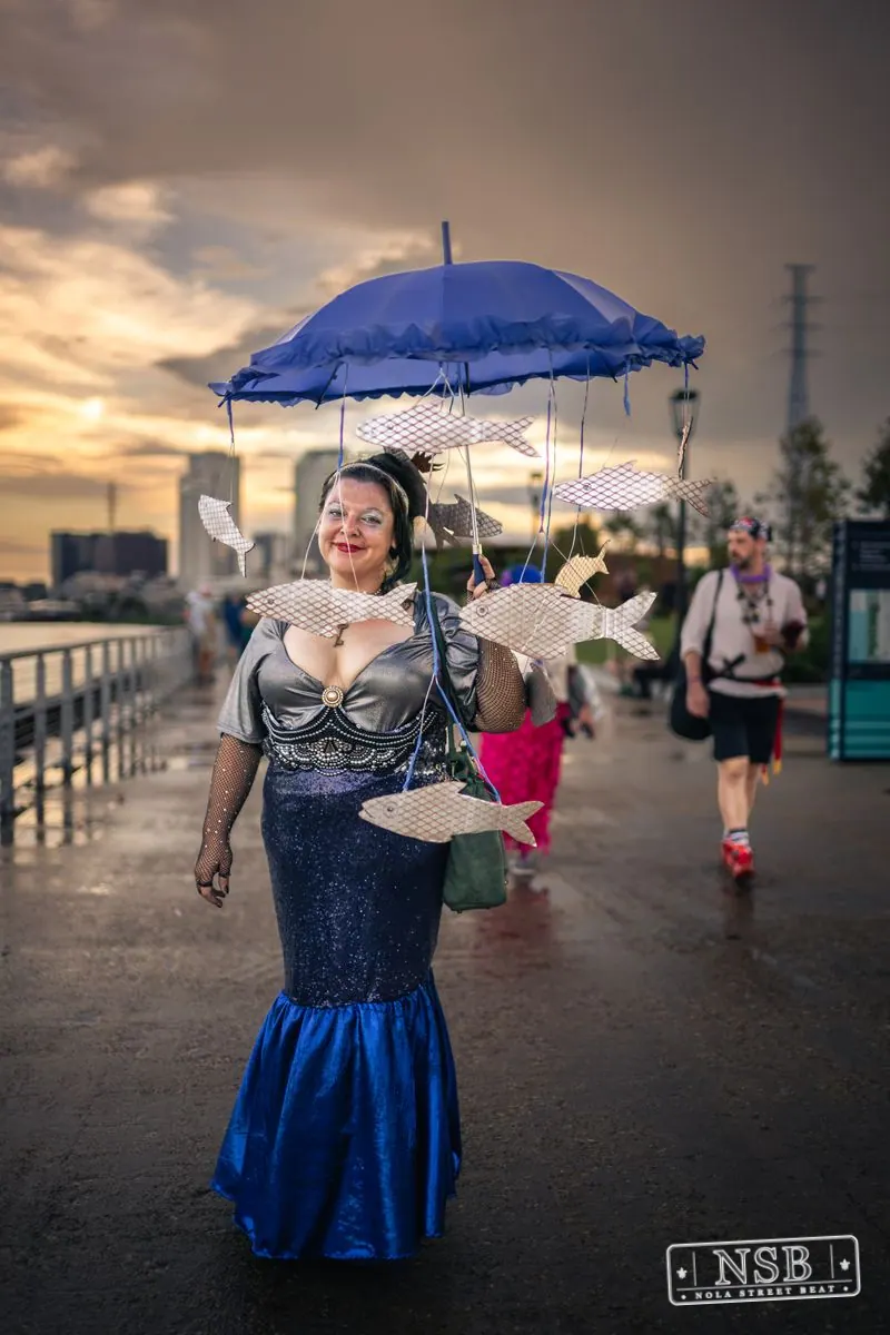 A participant in a blue mermaid costume holding a blue parasol at the 2026 New Orleans Mermaid Parade