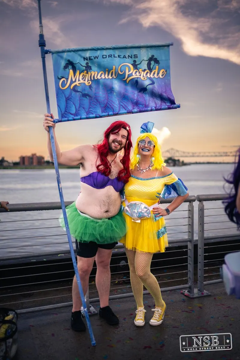 Two participants holding a New Orleans Mermaid Parade banner at the 2026 New Orleans Mermaid Parade
