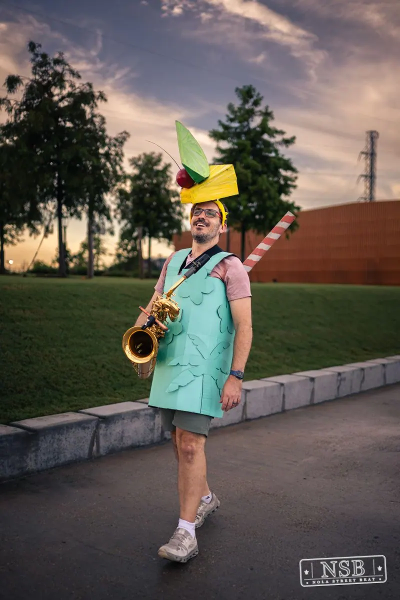 A costumed saxophonist beside the riverfront path at the 2026 New Orleans Mermaid Parade