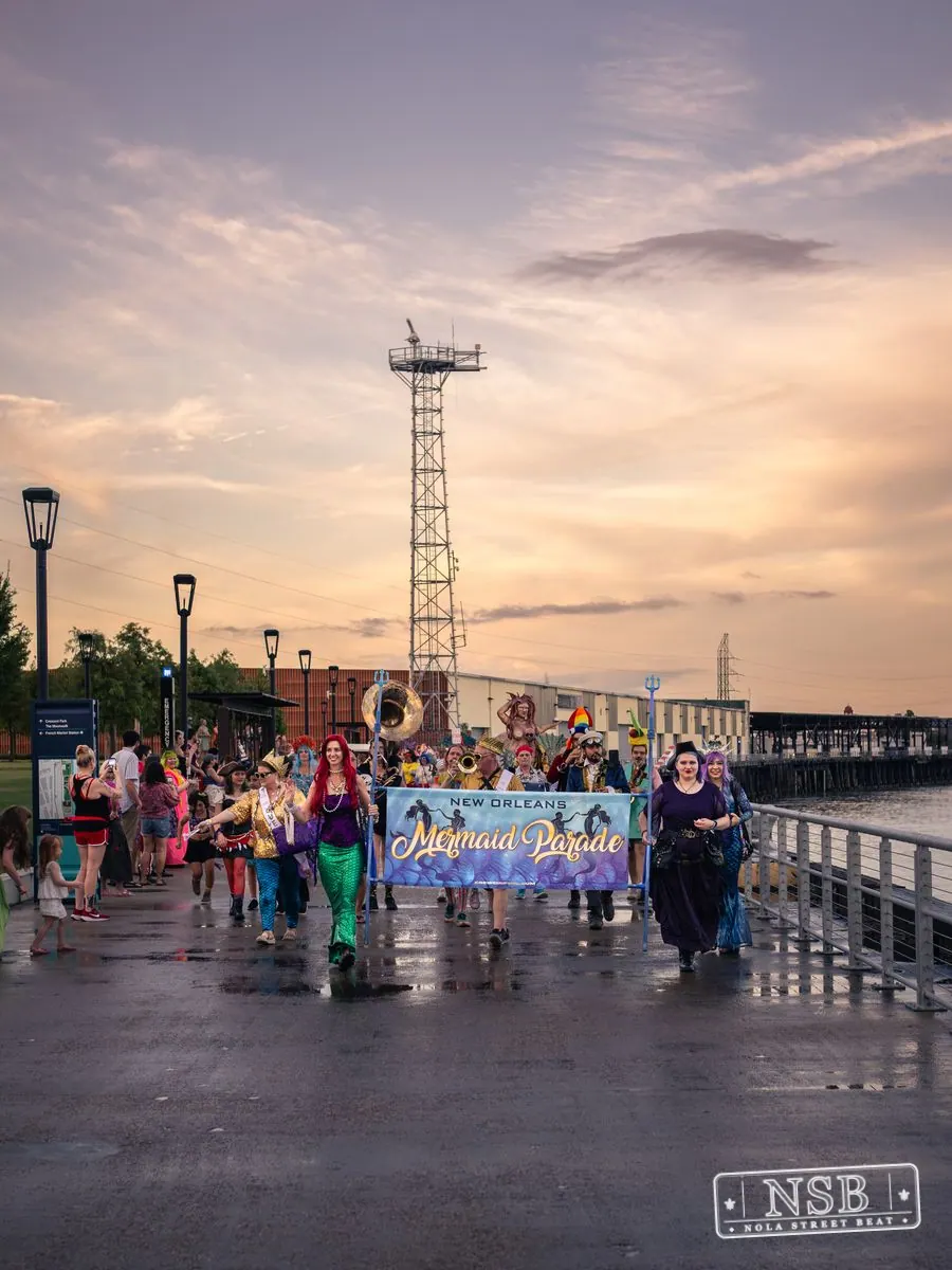 The Mermaid Parade gathering behind its banner on the riverfront promenade at the 2026 New Orleans Mermaid Parade