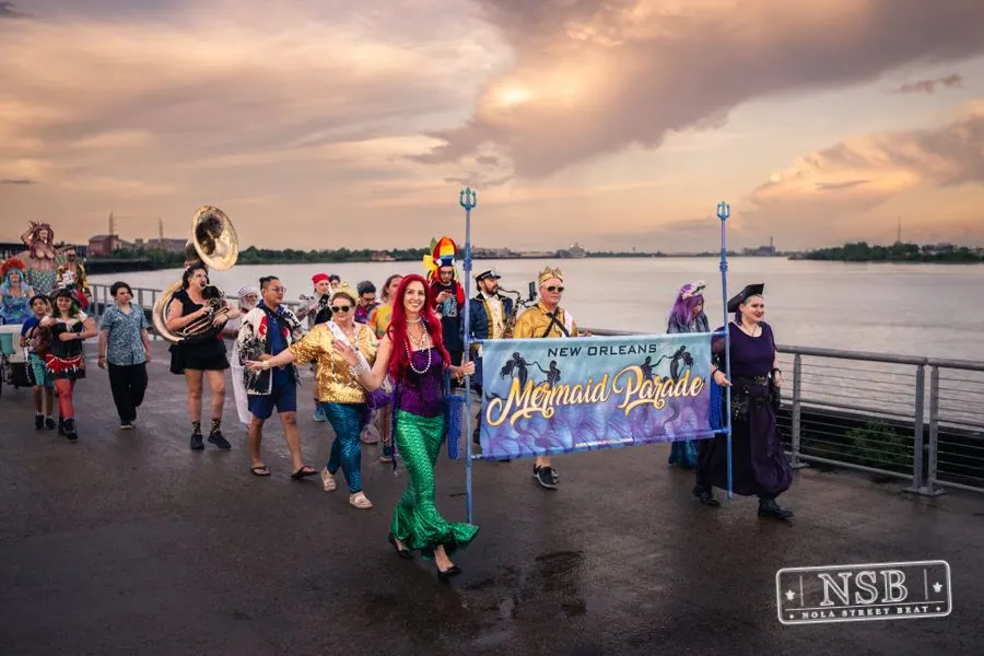 The Mermaid Parade banner leading costumed marchers along the Mississippi River at the 2026 New Orleans Mermaid Parade