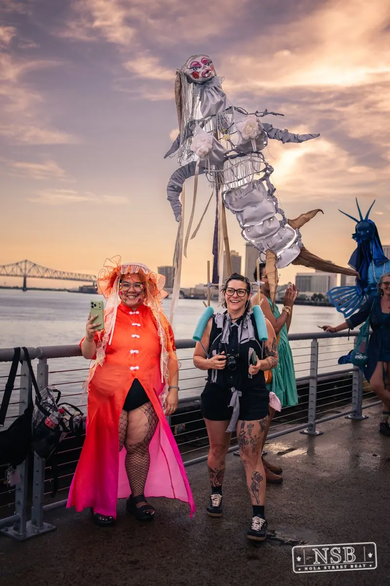 Costumed participants and a large seahorse figure beside the river at the 2026 New Orleans Mermaid Parade