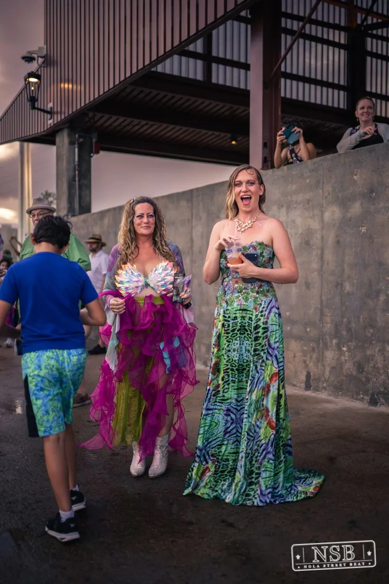 Two mermaid-costumed participants beside a riverfront pavilion at the 2026 New Orleans Mermaid Parade