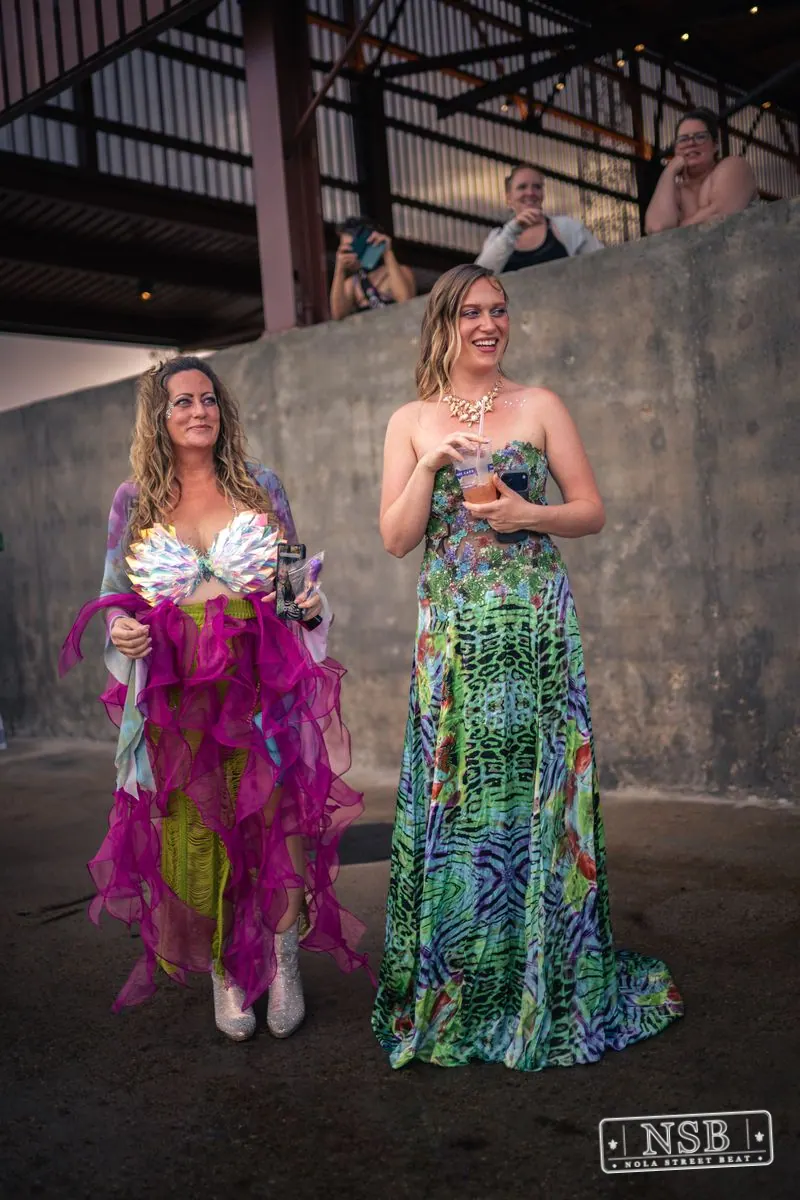 Two mermaid-costumed participants beside a riverfront pavilion at the 2026 New Orleans Mermaid Parade