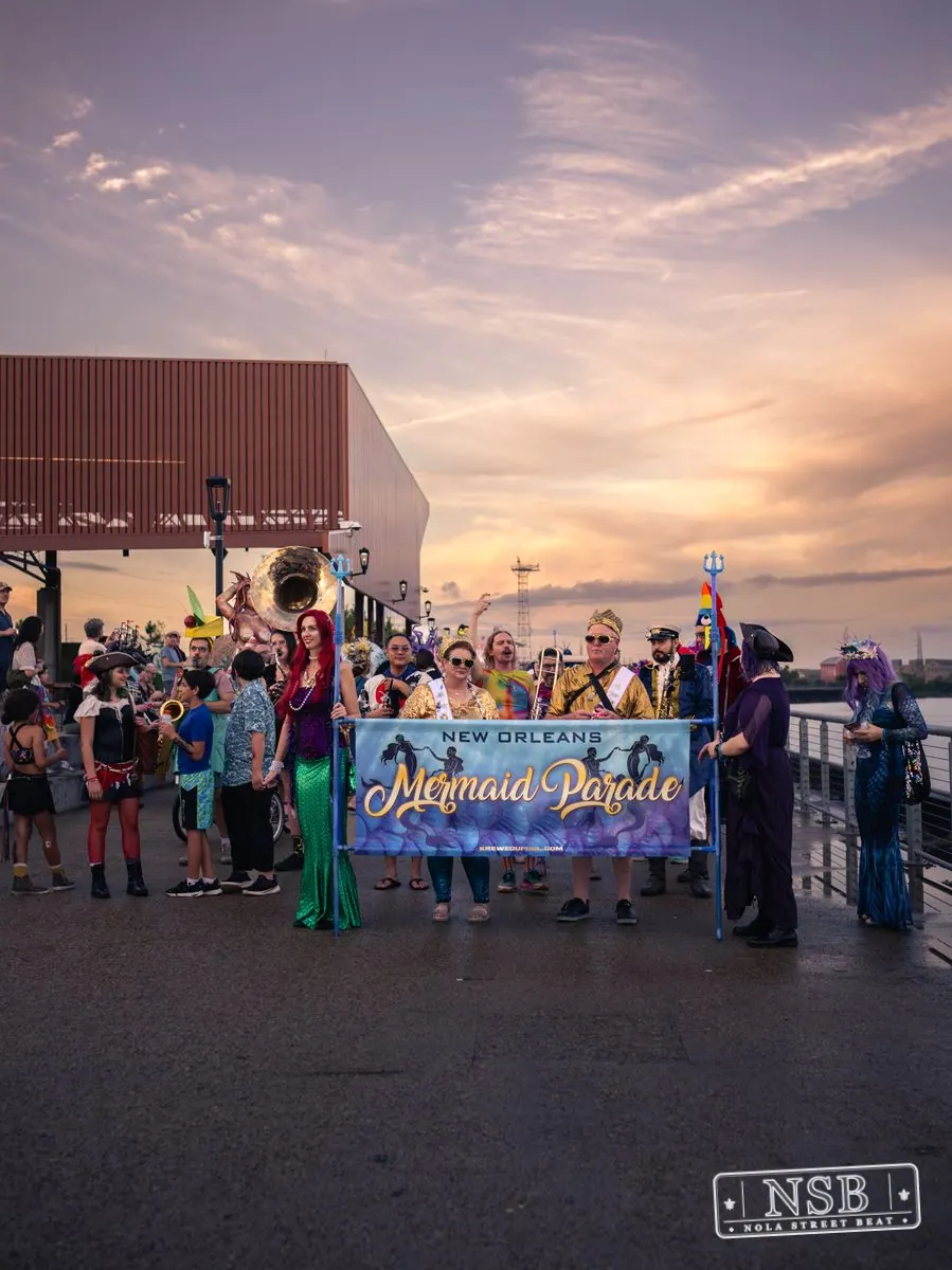 The Mermaid Parade approaching along the riverfront with its banner at the 2026 New Orleans Mermaid Parade