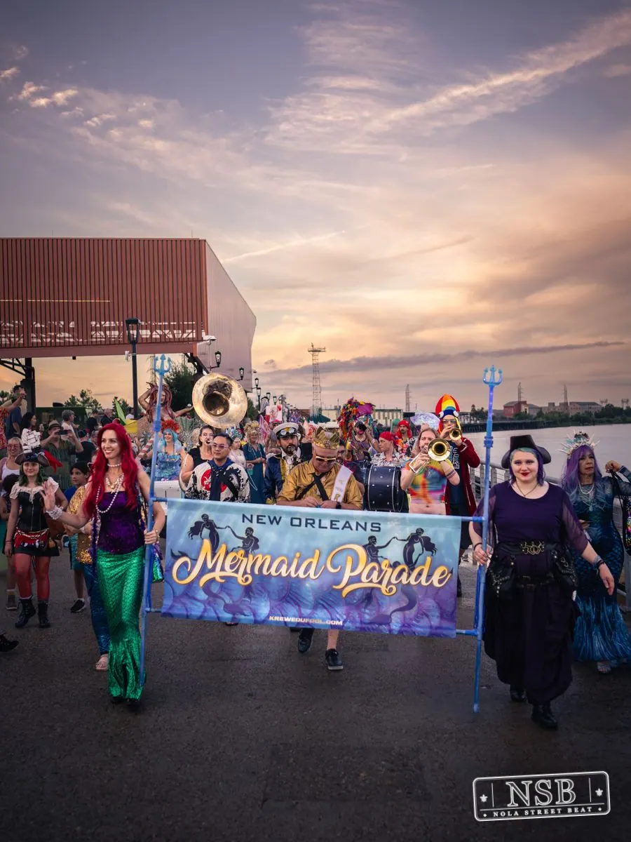 The Mermaid Parade approaching along the riverfront with its banner at the 2026 New Orleans Mermaid Parade