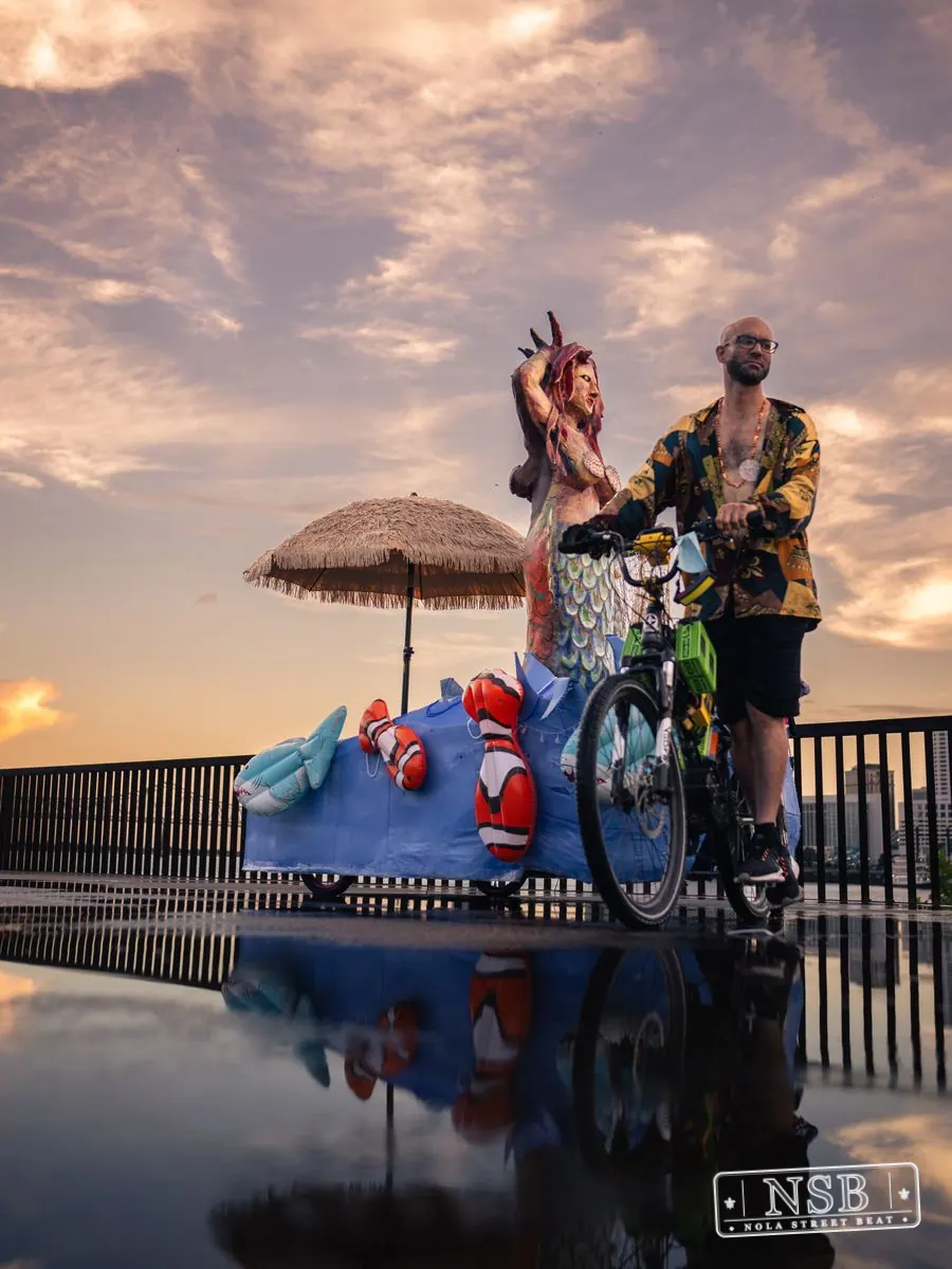 Large sea-themed figures and parade participants reflected on the wet promenade at the 2026 New Orleans Mermaid Parade