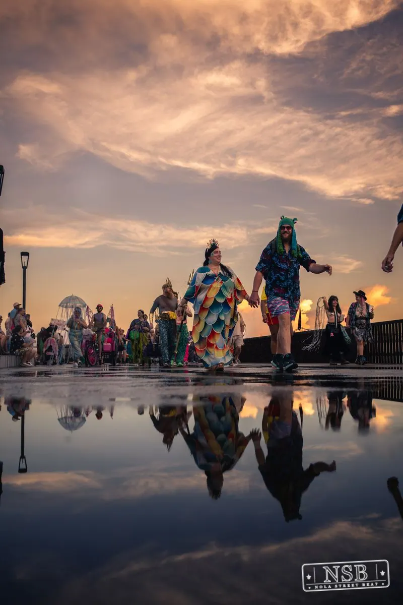 Large sea-themed figures and parade participants reflected on the wet promenade at the 2026 New Orleans Mermaid Parade