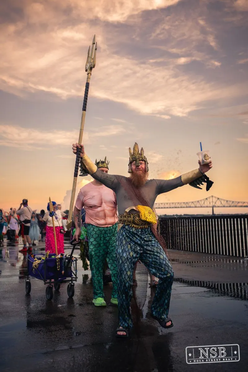 A crowned participant carrying a trident with the parade behind them at the 2026 New Orleans Mermaid Parade