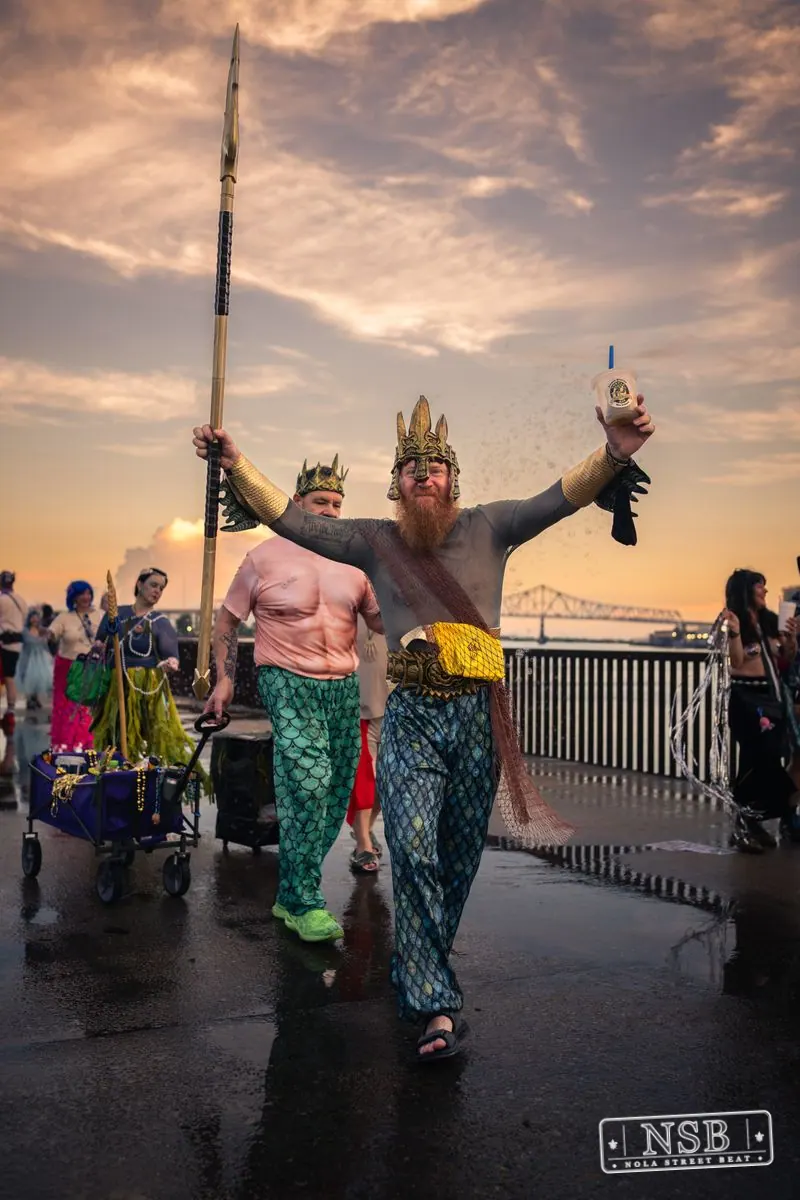 A crowned participant carrying a trident with the parade behind them at the 2026 New Orleans Mermaid Parade