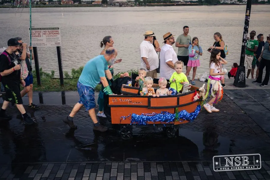 Participants pushing a decorated parade cart along the riverfront at the 2026 New Orleans Mermaid Parade