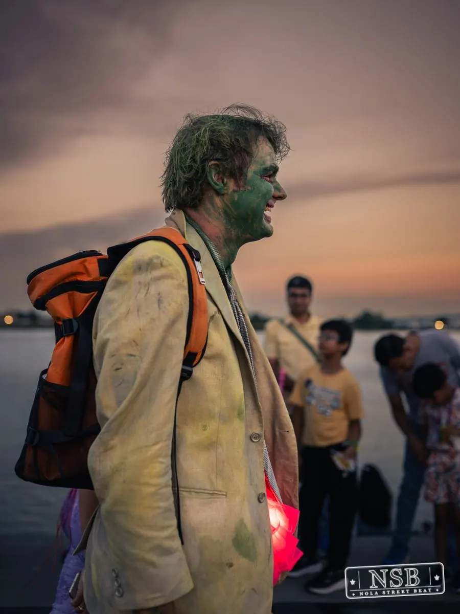 A participant in a green fish-inspired headpiece along the parade route at the 2026 New Orleans Mermaid Parade