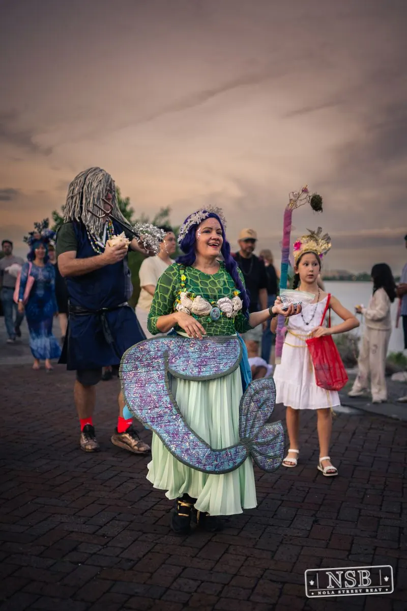 A green-costumed mermaid participant smiling during the parade at the 2026 New Orleans Mermaid Parade