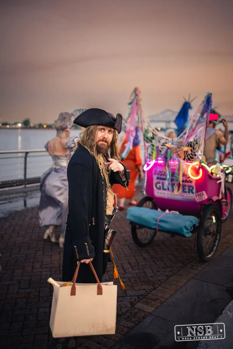 A pirate-costumed participant beside a decorated parade bicycle at the 2026 New Orleans Mermaid Parade