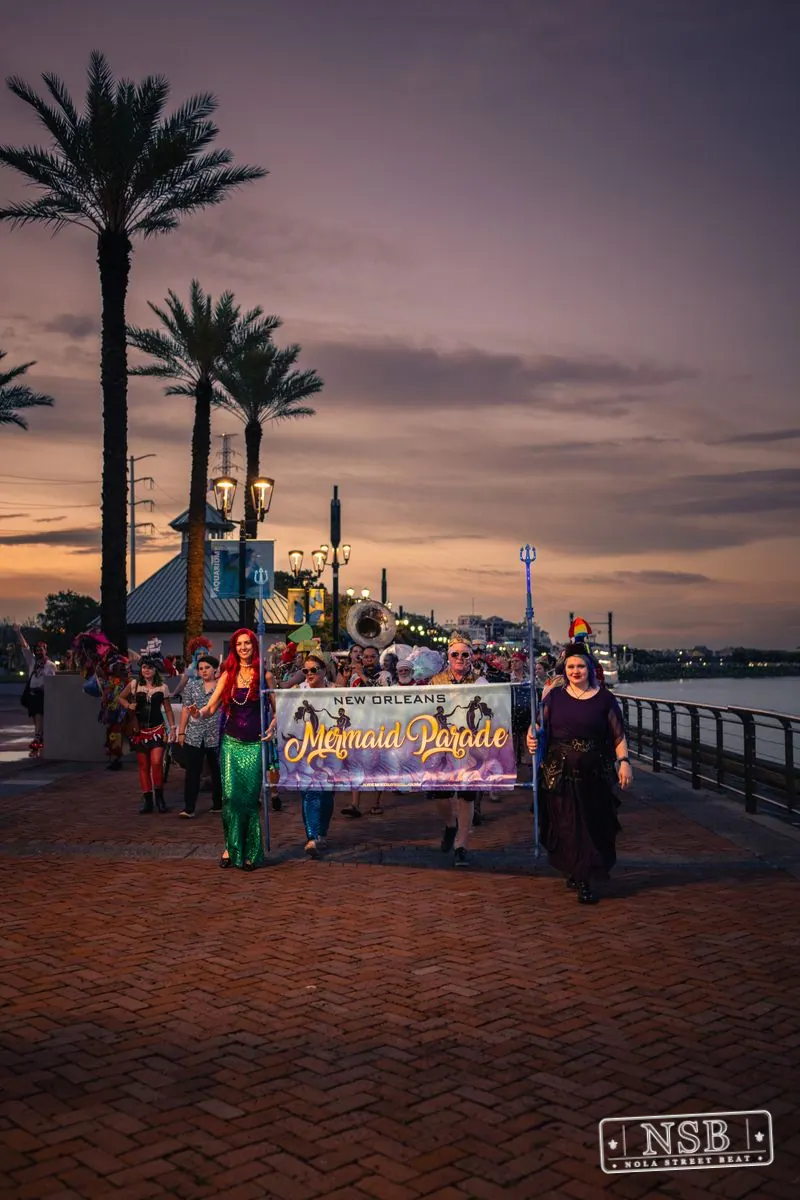 The Mermaid Parade continuing toward the Aquarium along the river at dusk at the 2026 New Orleans Mermaid Parade