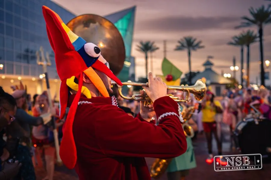 A parade participant wearing a bright orange fish headpiece at dusk at the 2026 New Orleans Mermaid Parade