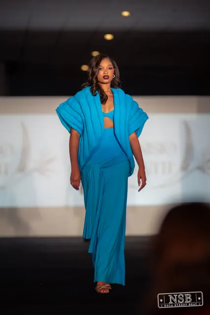 Turquoise pleated jumpsuit on the runway at New Orleans Fashion Week 2026. Photo 0061 by Nola Street Beat.