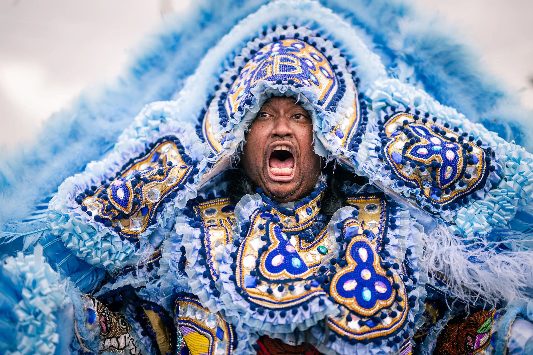 A Black Masking Indian in a detailed blue, white, and gold suit calling out during a New Orleans procession